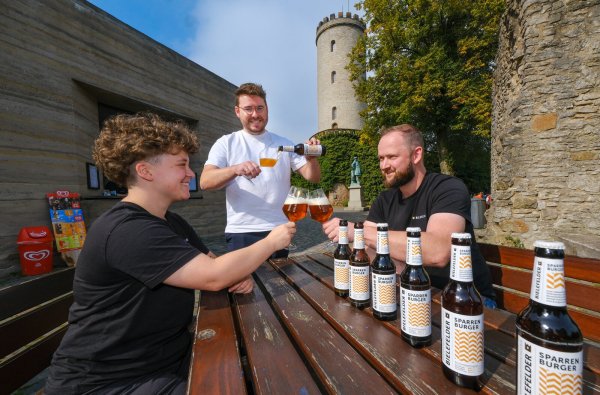 Paulina Comblain (v.l.), Mike Cacic und Torsten Vullriede kosten ihr neues „Sparrenburger“ am Kiosk der Burg. Dass das auf dem 52. Breitengrad genossene Bier 5,2 Prozent Alkohol hat, ist dann aber doch eher Zufall. Foto: Andreas Zobe - © Andreas Zobe