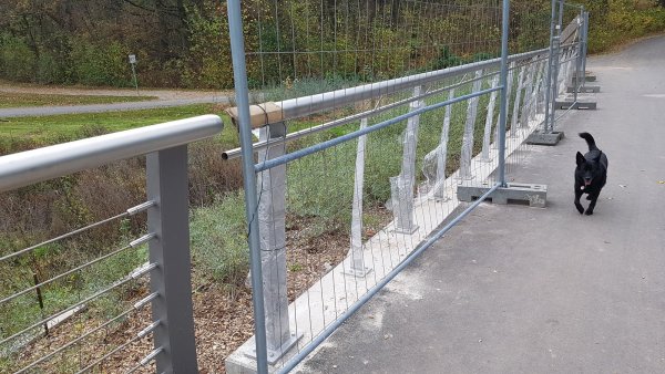 Über ein Jahr nach der Installation des Brückengeländers an der neuen Emmerbrücke für Radfahrer und Fußgänger wurde jetzt eine Ergänzung installiert. Noch schützt ein  Bauzaun die Konstruktion, weil die Stahlseile als Querverstrebung fehlen. - © Marianne Schwarzer