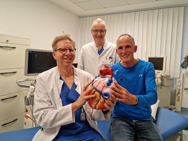Oberarzt Dr. Johannes Brockmeier (von links) und Chefarzt Dr. Stefan Gielen sind froh, dass es Friedrich-Wilhelm Althof heute wieder gut geht. Am Herzmodell zeigen Brockmeier und Althof die Lungenvenen in blau, die bei Althof verödet wurden, um sein Vorhofflimmern zu behandeln. - © Carolin Brokmann-Förster