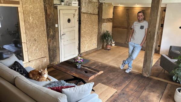 Murat Erbach mit Kater "Floki" im fertig sanierten Wohnzimmer des denkmalgeschützten Haupthauses seines Hofes - später, sobald die Diele fertig ist, werden die Gefache, die jetzt noch mit OSB-Platten verkleidet sind, geöffnet. - © Alexandra Schaller