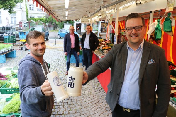 Maximilian Janski, Vorsitzender des Schötmaraner Bürgervereins, stößt mit Andreas Plaß, Vorsitzender des Wochenmarktvereins, an dessen Gemüsestand an. Im Hintergrund André Schröder, stellvertretender Vorsitzender des Bürgervereins (links) und Oliver Siekmann vom Stadtmarketing. - © Alexandra Schaller