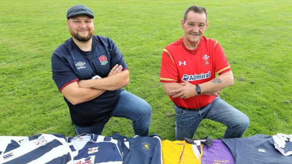 Die alten Trikots sind auf einer Bank fein aufgereiht – und Simon Chappell im England-Fan-Shirt sowie Pete James im roten Wales-Dress sind startklar für die K.o-Spiele bei der WM. - © Oliver König
