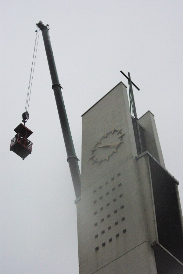 Mit viel Karabinerhaken, Seilen undweiterem Kletterzubehör am Gürtel werden die Spezialisten des Dachdeckerbetriebs mit der Gondel am Autokran auf die Kirchturmspitze gehievt. Dort müssen sie das riesige Kreuz sichern und anschlißeßend vom Turm abflexen. - © Dieter Asbrock