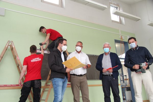 Joel Ollermann (von links) und Luca Klausing von der Firma Elektro Dresselhaus schrauben Kabelkanäle an die Wände eines Klassenzimmers, während Bauamtsleiter Manuel Bröker, Maik Czarnecki aus dem Fachbereich Bildung, Soziales und Sport, Bürgermeister Thomas Katzer und Kämmerer Patrick Herrmann einen Blick in die Pläne werfen. - © Nadine Uphoff