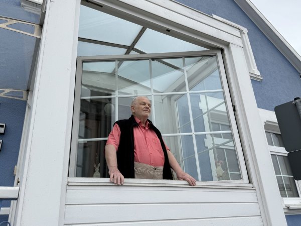 Der frühere Bundestagsabgeordnete Hans Verheyen im Windfang seines Hauses: Die riesigen Lüftungsanlagen auf dem Dach des benachbarten Lidl-Marktes an der Teutoburger Straße machen so viel Lärm, dass es durchs geschlossene Fenster zu hören ist, klagt er. - © Martin Krause
