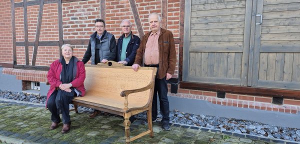 Petra Düe hat auf der alten Bank Platz genommen, die aufwendig restauriert wurde. Dirk Schneider (von links), Paul Fait und Hans-Jürgen von Boehn freuen sich, dass die alte Bank runderneuert zum Bahnhof Ehlenbruch zurückgekehrt ist. - © Ana Adzovic