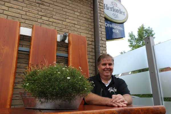Joachim Kroos, genannt „Apitz", sitzt in der Raucherecke seines Biergartens auf den urigen Holzbänken. - © Alexandra Schaller