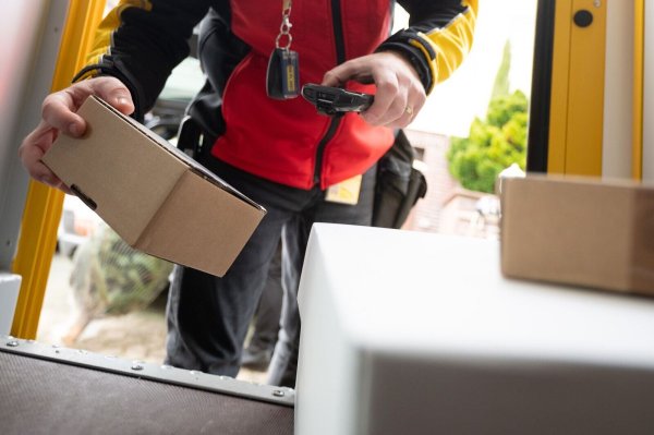 Ein DHL-Mitarbeiter scant ein Paket für die Zustellung. - © Sebastian Gollnow/dpa