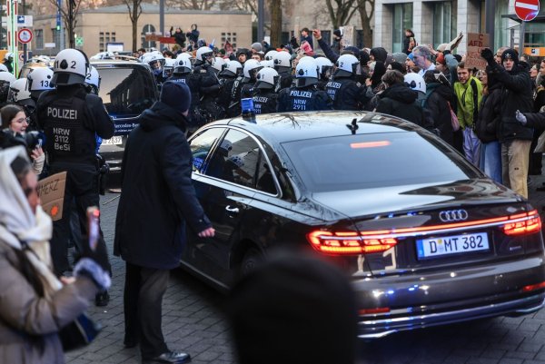 Polizisten schieben Demonstranten beiseite, damit Autos das Geländer der Kölner Uni-Klinik verlassen können. - © Oliver Berg/dpa