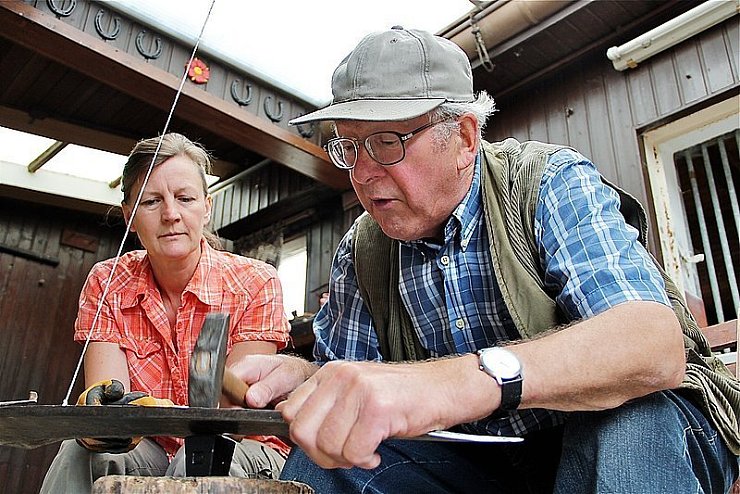 Beim Dengeln des Sensenblattes ist Präzisionsarbeit gefragt. Karin Radtke beobachtet jeden Handgriff von Friedel Elkenkamp. - © Foto: Stork