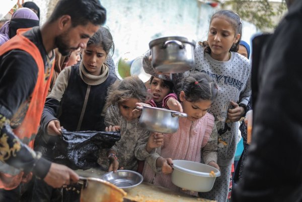 Menschen stehen in Rafah im Süden des Gazastreifens mit Töpfen, Schalen und Tüten bei einer Essensausgabe an. - © Mohammed Talatene/dpa