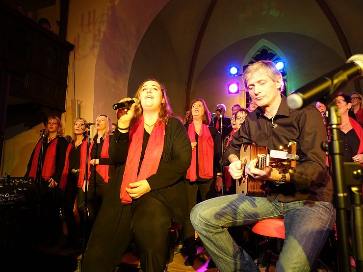 Überragend: Die stimmgewaltige Christina Friedrich (vorne links) wird von ihrem Chor auch „The Voice“ genannt. Gerd-Matthias Hoeffchen begleitet an der Gitarre. - © B-Joy!