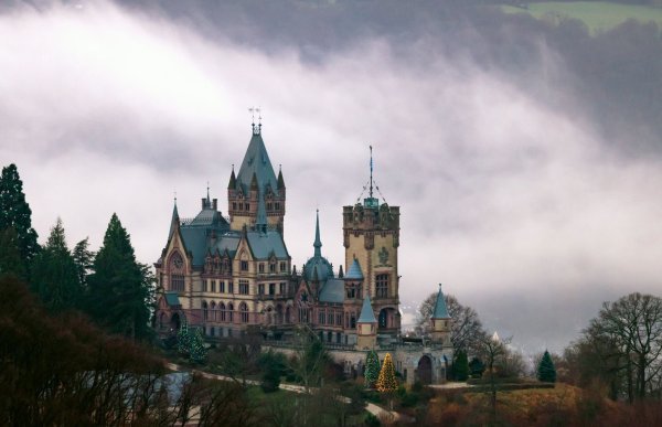 Weihnachtsbäume leuchten an der im Nebel liegenden Drachenburg. - © Thomas Banneyer/dpa