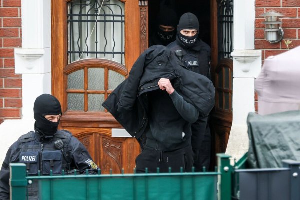 Polizeibeamte führen einen Tatverdächtigen aus einem durchsuchten Haus. - © Christoph Reichwein/dpa