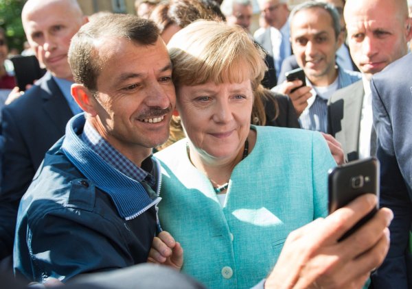 Bald zehn Jahre her: Angela Merkel (CDU) lässt sich nach dem Besuch einer Erstaufnahmeeinrichtung für Asylbewerber in Berlin-Spandau für ein Selfie zusammen mit einem Flüchtling fotografieren. (Archivbild) - © Bernd von Jutrczenka/dpa