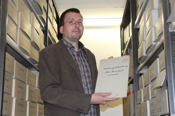 Blick in die Geschichte: Marcel Oeben, Leiter des Stadtarchivs Lemgo, zeigt im Magazin einen Ordner mit historischen Unterlagen zur Namensverleihung „Alte Hansestadt" vor 100 Jahren. - © Tobias Schneider