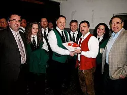 Andreas Jungwirt (rote Weste) überreicht die Noten für das Lied "Freunde der Blasmusik" an seinen Dirigentenkollegen Eerke van der Glas. Das freut auch die Bürgermeister Friedrich Ehlert (rechts) und Thomas Müller (links). - © Foto: Sölter