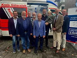 Thomas Kuhlbusch (v.l), Dezernent, Kreis G&uuml;tersloh, Detlef Vincke &Uuml;berlebender, Ralf Stroop, Entwickler und Ideengeber, Andreas Lekic, &Uuml;berlebender, Heinrich Harbrock, &Uuml;berlebender, Alexander Bloch, &Uuml;berlebender, und Bernd Strickmann, &Auml;rztlicher Leiter des kreiseigenen Rettungsdienstes, feiern gemeinsam mit Landrat Sven-Georg Adenauer (2.v.r.) vor dem Kreishaus. - &copy; Danielle D&ouml;rsing
