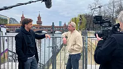Tommi Schmitt (links) interviewt Robin Gosens in Berlin. Sie stehen am Ufer der Spree, hinter ihnen liegt die Oberbaumbr&uuml;cke. Neben ihnen steht ein Kameramann, ein Tonarm mit Mikrofon ragt in das Bild. - &copy; ZDF und Gruppe 5