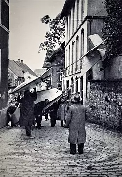 Eine spektakul&auml;re Situation spielte sich vor dem langen Gottfried, rechts, in den 1930-er Jahren ab. Segelflugsch&uuml;ler hatten ein Flugzeug in einer Werkstatt gebaut und transportierten es zum Flugplatz - hochkant durch die enge Stelle der Hauptstra&szlig;e. Im Vordergrund: Fritz (&bdquo;Tempo&ldquo;) Drewes. - &copy; Repro: Horst Biere