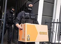 Ein Polizist trägt im Rahmen der Razzia gegen die Schleuser-Bande einen Karton aus einem Gebäude (Archivfoto) - © Benjamin Westhoff/dpa