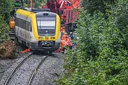 Mit einem Kran wird an der Unfallstelle, an der ein Regionalzug entgleist ist, gearbeitet. Ein Regionalexpress war am Sonntagabend (27.07.2025) in Riedlingen nach bisherigen Erkenntnissen infolge eines Hangrutsches entgleist. - &copy; Jason Tschepljakow/dpa
