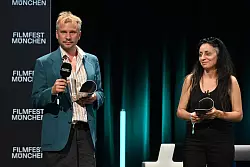 Schauspieler Robert Stadlober steht mit seinem Publikumspreis f&uuml;r den Film &laquo;F&uuml;hrer und Verf&uuml;hrer&raquo; neben der Regisseurin Yasemin Samdereli, die f&uuml;r den Film &laquo;Samia&raquo; bei der Preisverleihung im Rahmen des Filmfest M&uuml;nchen ausgezeichnet wurde. - &copy; Felix H&ouml;rhager/dpa