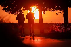 Zwei Frauen joggen am Morgen, während hinter ihnen die Sonne aufgeht. - © Thomas Warnack/dpa