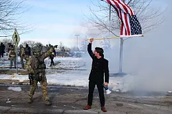 Ein Protestierender mit einer amerikanischen Flagge steht einem ICE-Beamten gegen&uuml;ber. - &copy; Adam Bettcher/AP/dpa
