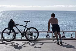 Ein Mann mit nacktem Oberkörper macht am Strand von Nizza neben seinem Fahrrad Übungen. (Archivbild) - © Serge Haouzi/XinHua/dpa