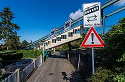 Die 1901 gebaute Schwebebahn f&auml;hrt zum Dresdner Stadtteil Oberloschwitz &uuml;ber einer Stra&szlig;e an einem Warnschild vorbei. (Archivbild) - &copy; Robert Michael/dpa-Zentralbild/dpa