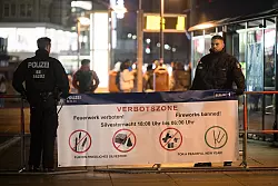 Polizeibeamte stehen an einem Plakat, das auf die Böllerverbotszone am Berliner Alexanderplatz hinweist. - © Sebastian Christoph Gollnow/dpa