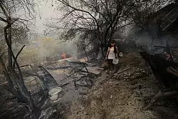 Ein Mann geht an einem Haus vorbei, das bei einem Waldbrand in der algerischen Provinz Bouira niedergebrannt ist. - &copy; XinHua/dpa