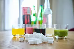 Fünf unterschiedliche Arten Softdrinks und die Flaschen dazu zusammen mit Zuckerwürfel auf einem Tisch - © Annette Riedl/dpa