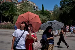 Touristen schützen sich amvor der Kirche Sagrada Familia mit Regenschirmen vor der Sonne. - © Emilio Morenatti/AP/dpa