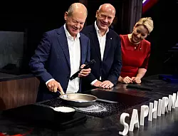 An einem Stand wurde Scholz, Wegner und Giffey ein Kochfeld gezeigt, dass unempfindlicher gegen Kratzer sein soll. - © Carsten Koall/dpa