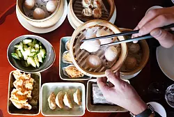 Ein Mann greift mit Essst&auml;bchen nach Dim sum, ged&auml;mpften Teigtaschen, in einem Bambuskorb. - &copy; Marcus Brandt/dpa