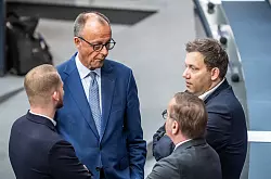 Vers&ouml;hnliche Tonlage: Kanzler Merz spricht mit SPD-Generalsekret&auml;r Kl&uuml;ssendorf (links) und SPD-Chef Klingbeil (ganz rechts) im Bundestag. (Archivbild) - &copy; Michael Kappeler/dpa