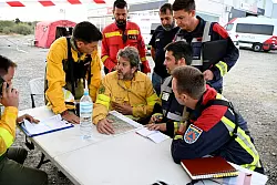 Spanische und aus Deutschland zur Hilfe geeilte Feuerwehrleute beraten bei dem Ort Jarilla über die Bekämpfung eines großen Waldbrandes. (Archivbild) - © Sven Käuler/dpa