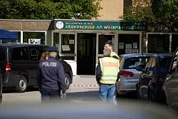 Polizisten stehen vor einer Schule in Spandau, an der es am Donnerstag einen Messerangriff auf einen Schüler gab. - © Jörg Carstensen/dpa