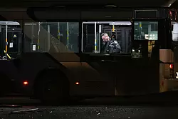 Ein Polizeibeamter inspiziert einen Bus. - © Ohad Zwigenberg/AP/dpa