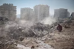 Ein Mann sitzt neben seinem eingest&uuml;rzten Haus, w&auml;hrend ein Suchteam in Kharamanmaras nach Menschen sucht. - &copy; Ahmed Deeb/dpa
