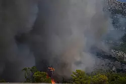 Ein Feuerwehrhubschrauber wirft Wasser auf die Flammen nahe des Milit&auml;rst&uuml;tzpunkts Kapota im Gebirge Parnitha. - &copy; Thanassis Stavrakis/AP/dpa