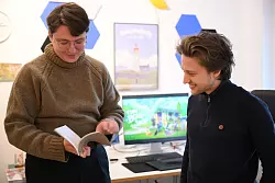 Zapfe-Wildemann hält ein Heft in der Hand, in dem Regeln für eine analoge Version von «Tiny Bookshop» stehen. - © Wolf von Dewitz/dpa