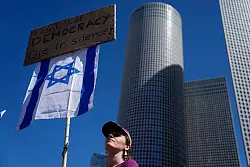 Eine Demonstrierende h&auml;lt eine israelische Fahne und ein Plakat mit der Aufschrift &laquo;Don\\\'t let Democracy die in silence!". - &copy; Ariel Schalit/AP/dpa