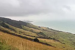 Nach fünf Stunden Fußweg tut sich hinter einem grünen Hügel das Ziel auf: Eastbourne liegt verwaschen da. - © Nathalie Helene Rippich/dpa-tmn