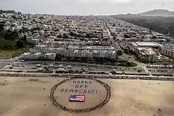 An einem Strand im Bundesstaat Kalifornien bildeten Demonstranten einen menschlichen Kreis um eine US-Flagge und den Slogan «Hände weg von der Demokratie!». - © Stephen Lam/San Francisco Chronicle/AP/dpa
