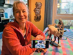 Krippenkünstlerin Annette Hiemenz sitzt an ihrer «Werkbank», dem Küchentisch, und präsentiert einige ihrer jüngsten Krippenfiguren. Auf dem Mobiltelefon zeigt sie ein Foto der noch unfertigen Kinderfiguren, die Bestandteil ihres Exponates für die 85. Telgter Krippenkunst-Ausstellung sind. - © Volker Danisch/dpa