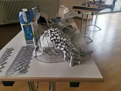 Ein kunstvoller Helm, der aus alten Milcht&uuml;ten gebastelt wurde, liegt auf einem Tisch. - &copy; Ramona Wahner/Deutsche Fastnachtakademie/dpa