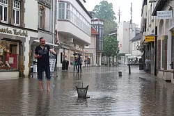 Galgenhumor im Salzufler Innenstadt-See: Geschäftsinhaber Matthias Herlitzius steht barfuß auf der Steege. Mit vereinten Kräften haben die Kaufleute die Abflüsse geöffnet, damit die Wassermassen besser ablaufen können. Auf dem Bild ist der Maximal-Pegel vom Donnerstag schon wieder gesunken. - © Stefan Backe